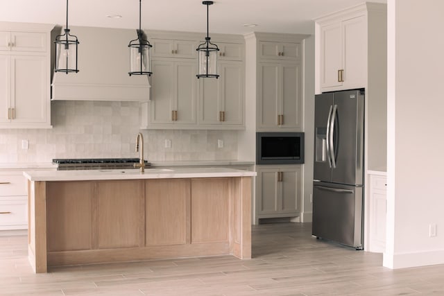 kitchen with a kitchen island with sink, stainless steel appliances, hanging light fixtures, and light hardwood / wood-style flooring