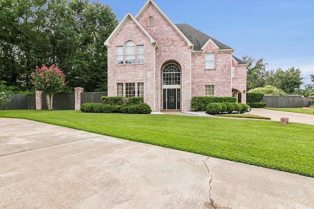 traditional-style house featuring a shingled roof, fence, a front lawn, and brick siding