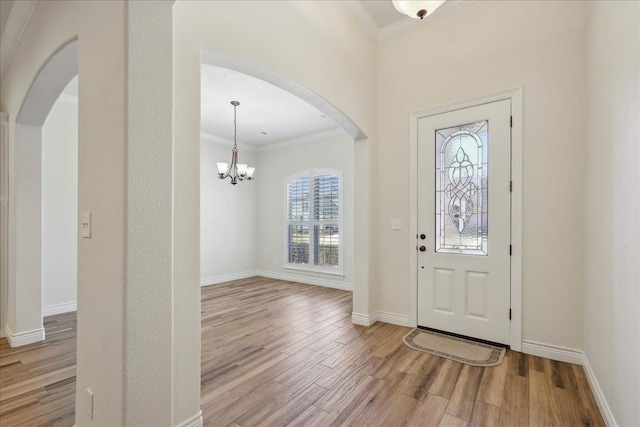 foyer featuring arched walkways, wood finished floors, baseboards, and ornamental molding