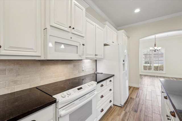 kitchen featuring dark countertops, light wood finished floors, crown molding, arched walkways, and white appliances