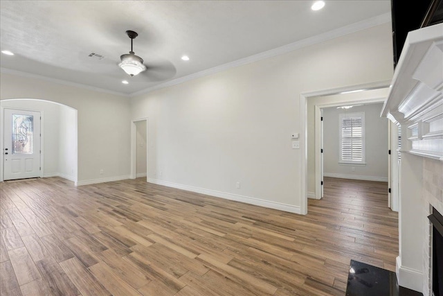 unfurnished living room with arched walkways, light wood-style flooring, a fireplace, and a ceiling fan