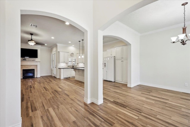 unfurnished living room featuring visible vents, crown molding, baseboards, light wood-style flooring, and a notable chandelier