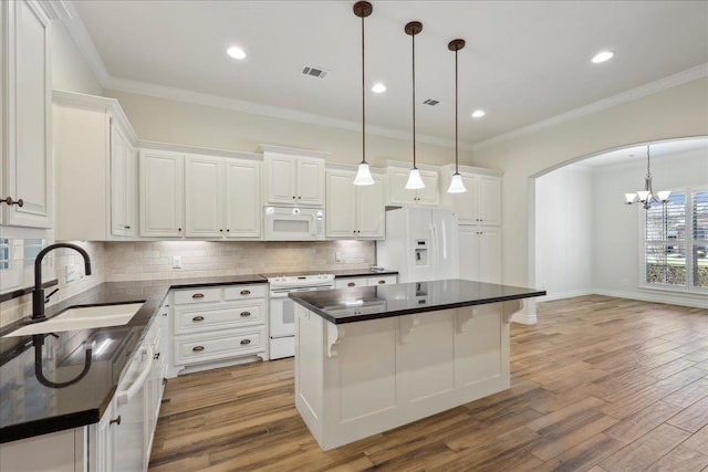 kitchen with a sink, white appliances, dark countertops, and arched walkways