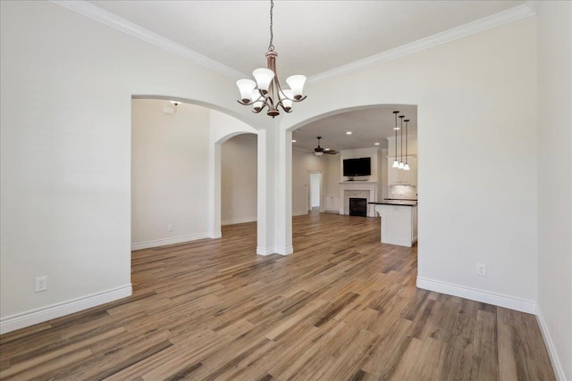 unfurnished dining area featuring wood finished floors, crown molding, a fireplace, and arched walkways