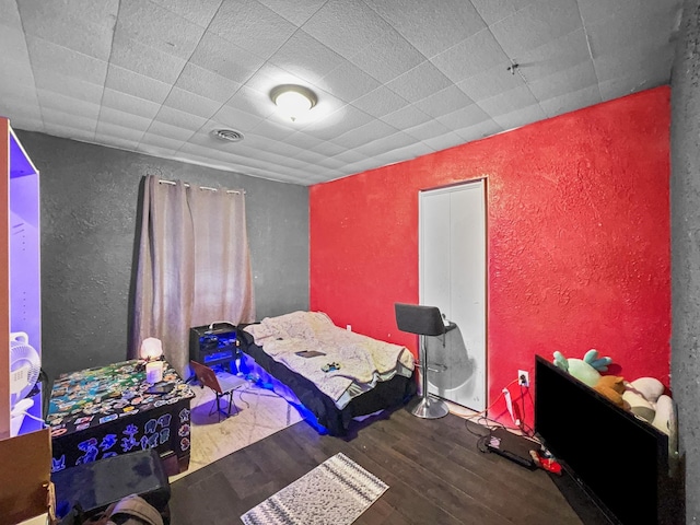 bedroom featuring visible vents, wood finished floors, and a textured wall