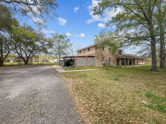 view of front of property featuring an attached carport, a front lawn, brick siding, and driveway