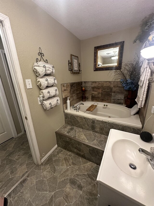 bathroom with vanity, a textured ceiling, and tiled bath