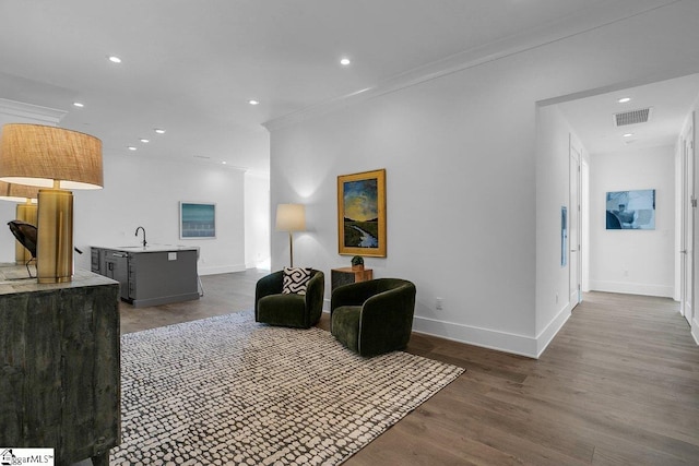 living room featuring wood-type flooring, crown molding, and sink