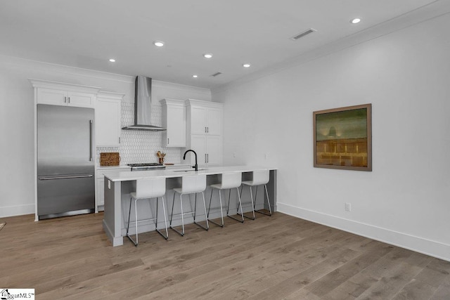 kitchen featuring white cabinetry, stainless steel built in fridge, wall chimney exhaust hood, and light hardwood / wood-style flooring