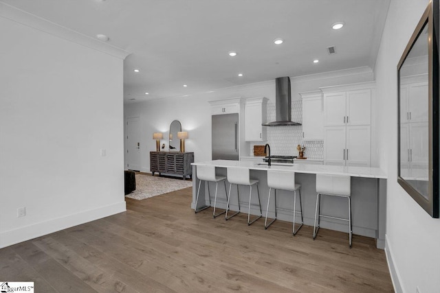 kitchen with white cabinets, wall chimney exhaust hood, a breakfast bar area, and light hardwood / wood-style flooring