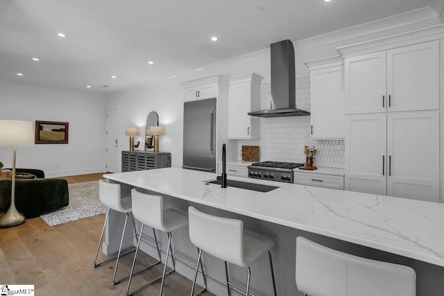 kitchen featuring a kitchen bar, light wood-type flooring, sink, wall chimney range hood, and white cabinetry