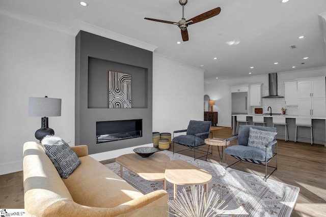 living room featuring light wood-type flooring, a large fireplace, ornamental molding, and sink