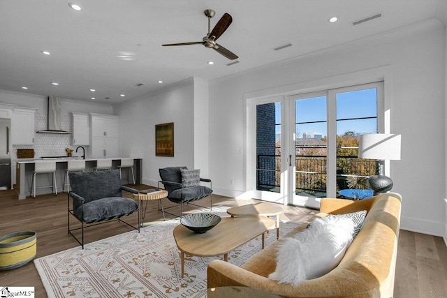 living room with light wood-type flooring, ceiling fan, ornamental molding, and sink