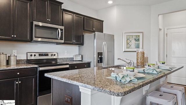 kitchen featuring an island with sink, a kitchen breakfast bar, appliances with stainless steel finishes, light stone counters, and sink