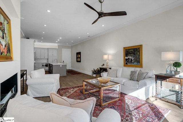 living room featuring ceiling fan, hardwood / wood-style floors, ornamental molding, and sink