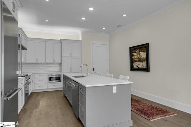 kitchen featuring sink, premium appliances, backsplash, a center island with sink, and light wood-type flooring