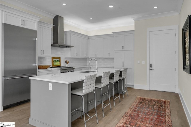 kitchen with a breakfast bar, a center island with sink, sink, wall chimney exhaust hood, and appliances with stainless steel finishes