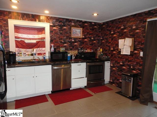 kitchen with white cabinetry, light tile flooring, brick wall, sink, and stainless steel appliances