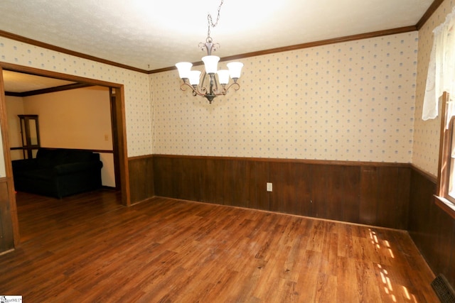 empty room with a notable chandelier, crown molding, and dark wood-type flooring