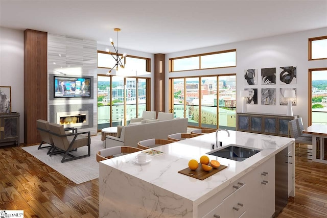 kitchen featuring an island with sink, a notable chandelier, pendant lighting, sink, and a large fireplace