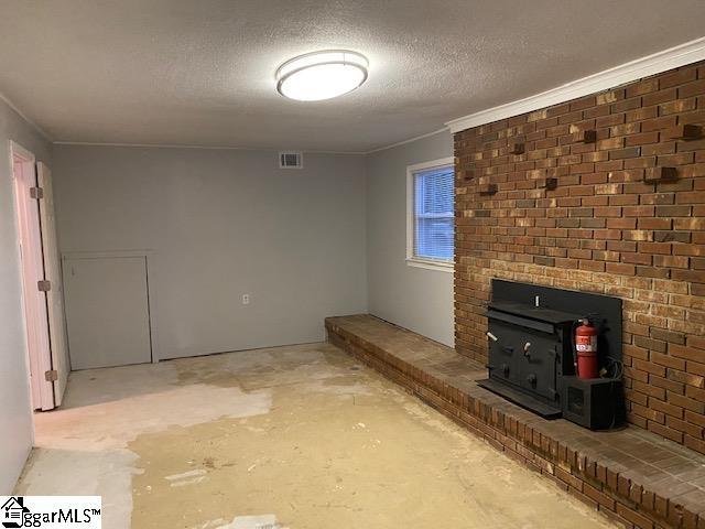 unfurnished living room featuring brick wall, a wood stove, a textured ceiling, and crown molding