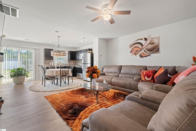 living room with ceiling fan with notable chandelier and light hardwood / wood-style flooring