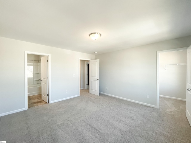 unfurnished bedroom with a closet, ensuite bath, light carpet, and a spacious closet