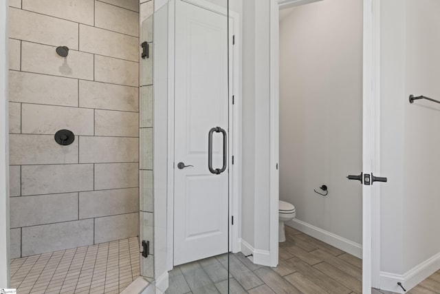 full bathroom with wood finish floors, baseboards, a shower stall, and toilet