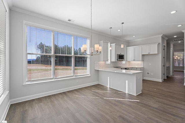 kitchen with a peninsula, white cabinetry, light countertops, hanging light fixtures, and stainless steel microwave