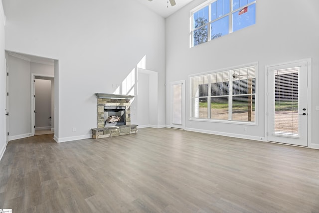 unfurnished living room with ceiling fan, a stone fireplace, plenty of natural light, and wood finished floors