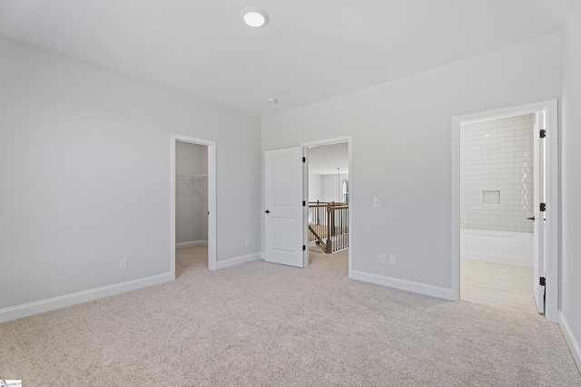 unfurnished bedroom featuring ensuite bathroom, light colored carpet, baseboards, a spacious closet, and a closet