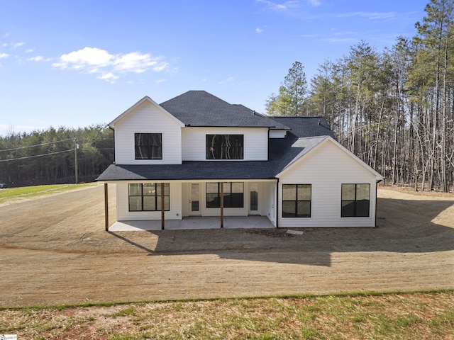 rear view of house with a patio area and roof with shingles