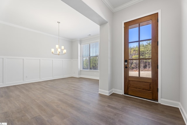 entrance foyer with a wainscoted wall, a notable chandelier, crown molding, a decorative wall, and wood finished floors