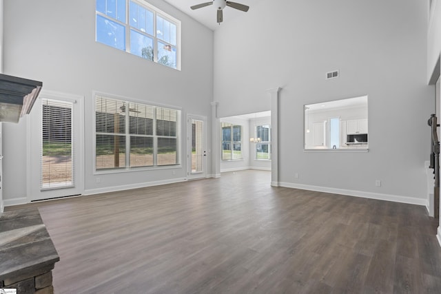 unfurnished living room featuring a ceiling fan, visible vents, dark wood-type flooring, and a wealth of natural light