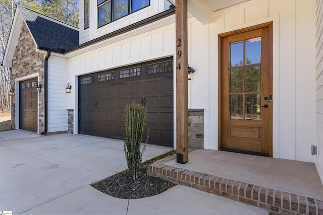 entrance to property with driveway, a garage, a shingled roof, stone siding, and board and batten siding