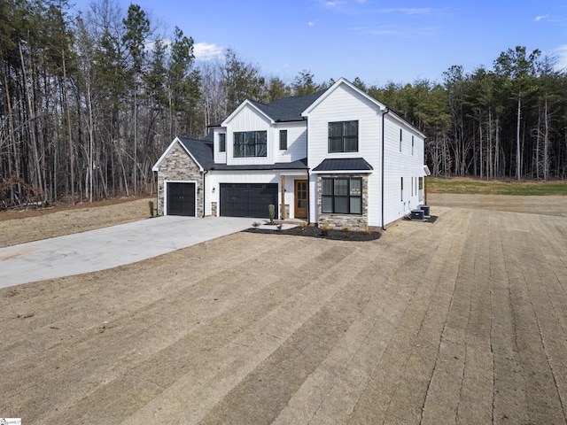 modern farmhouse featuring driveway, stone siding, and a wooded view