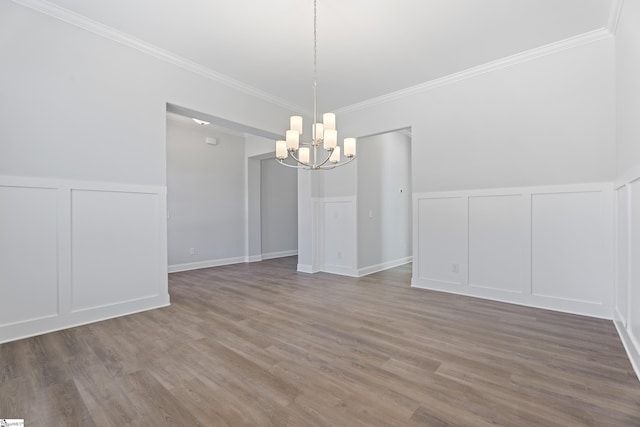 unfurnished dining area with a chandelier, ornamental molding, wood finished floors, and a decorative wall