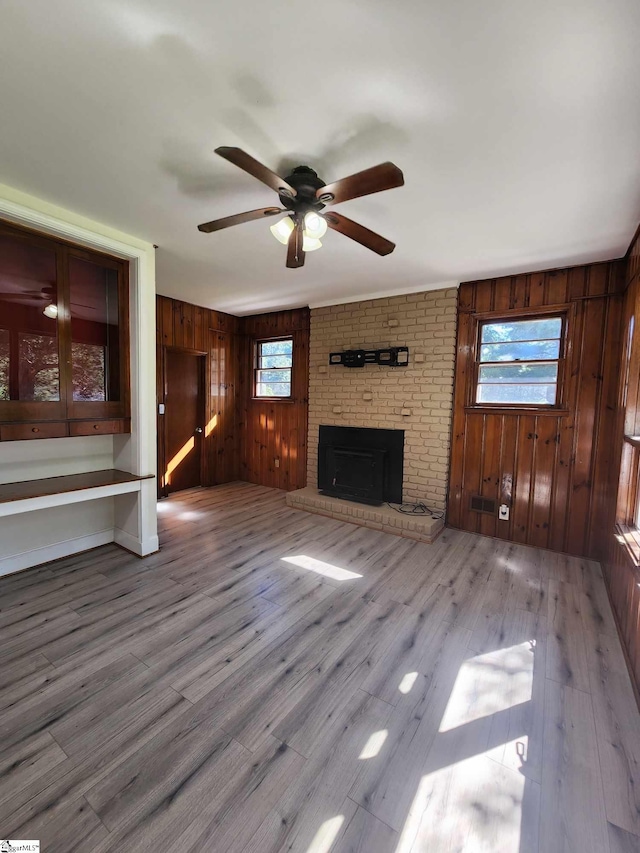 unfurnished living room featuring ceiling fan, a fireplace, brick wall, light hardwood / wood-style flooring, and wood walls