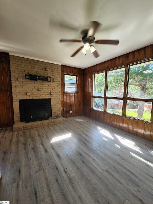 unfurnished living room featuring ceiling fan, wooden walls, a fireplace, dark hardwood / wood-style flooring, and brick wall