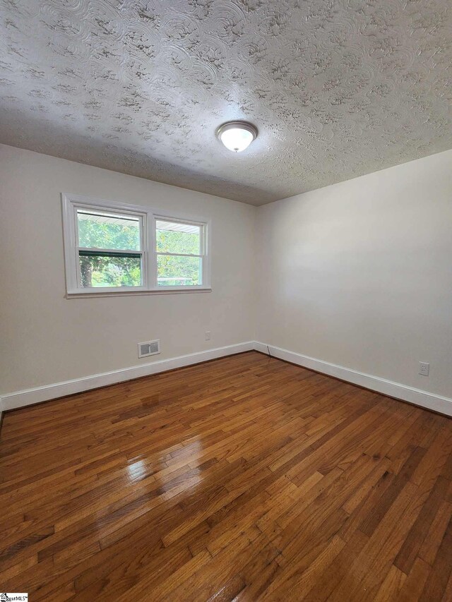 unfurnished room featuring a textured ceiling and dark hardwood / wood-style floors