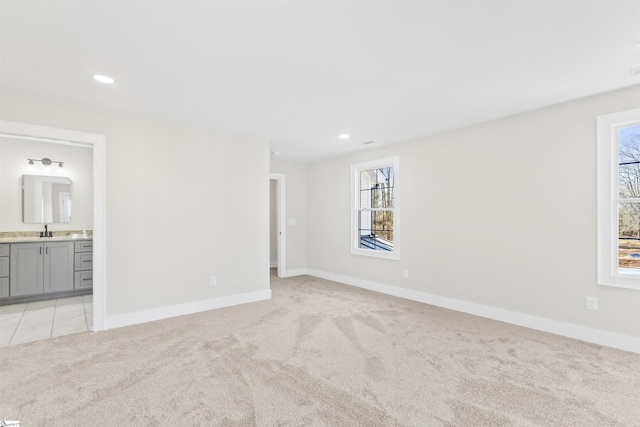 unfurnished bedroom featuring ensuite bathroom, sink, and light colored carpet