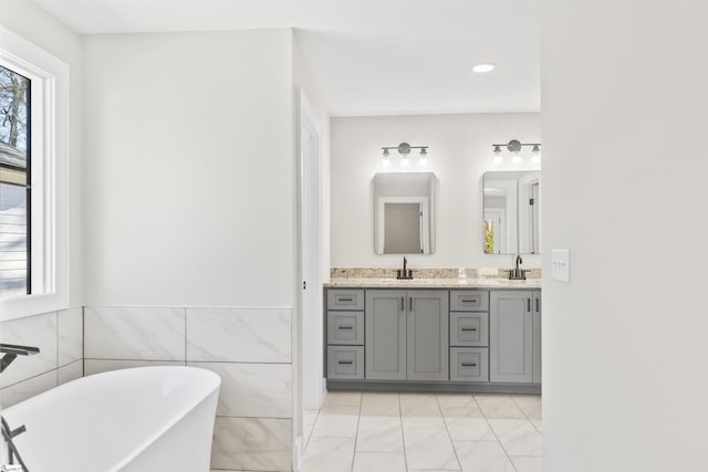 bathroom featuring plenty of natural light, a tub, vanity, and tile walls