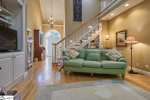 living room with a towering ceiling, a chandelier, and light hardwood / wood-style floors