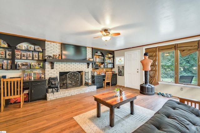 living room featuring ceiling fan, ornamental molding, a fireplace, and light wood-type flooring