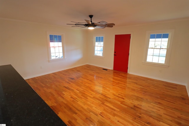 empty room with a wealth of natural light, ornamental molding, ceiling fan, and light wood-type flooring