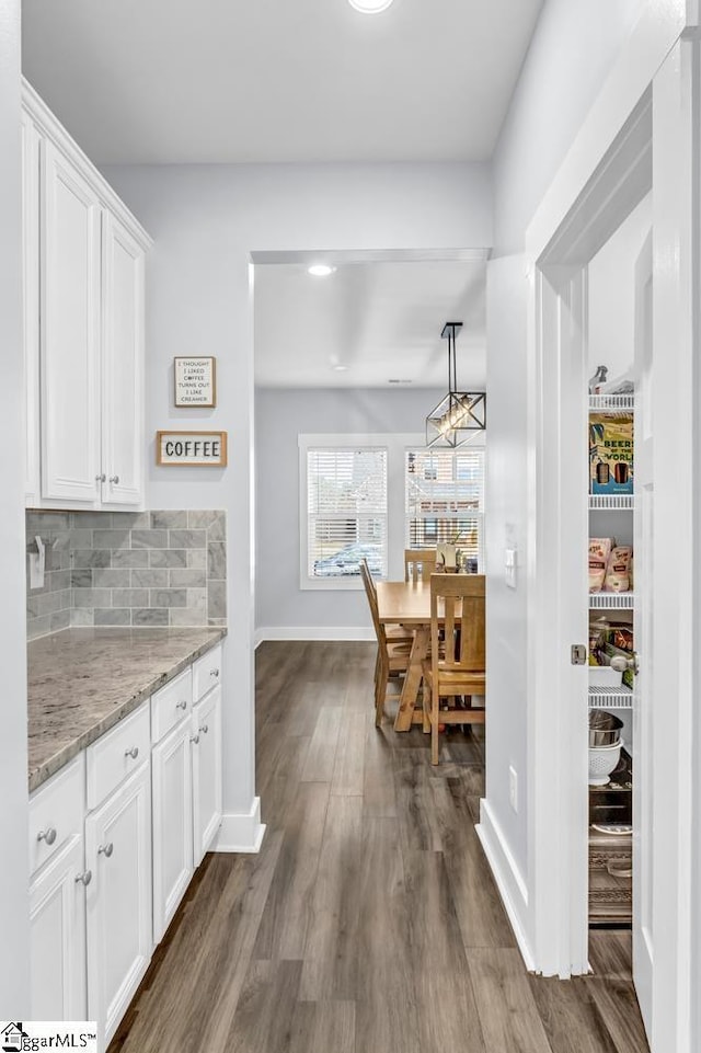 kitchen with light stone counters, dark hardwood / wood-style flooring, pendant lighting, decorative backsplash, and white cabinets