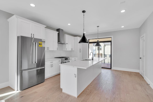 kitchen featuring a center island with sink, premium appliances, white cabinetry, and wall chimney range hood