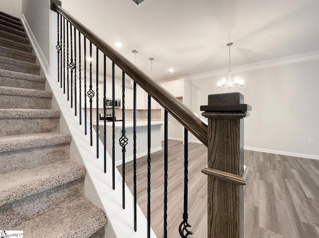 staircase with ornamental molding, wood-type flooring, and a notable chandelier