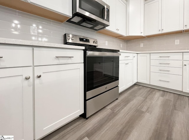 kitchen with tasteful backsplash, light wood-type flooring, stainless steel appliances, light stone countertops, and white cabinets