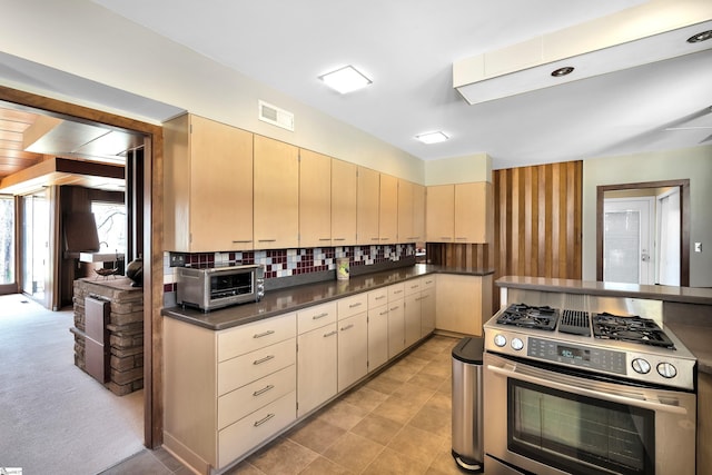 kitchen with light brown cabinetry, backsplash, stainless steel gas stove, and light colored carpet